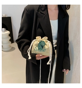 Detail of straw woven bucket bag featuring green Summer embroidery and drawstring closure