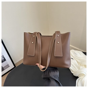 Detail of dark brown leather tote bag with golden rivets and contrast stitching accents