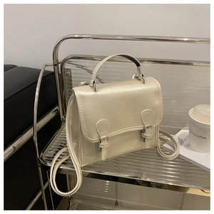 Detailed view of a cream-colored top-handle bag on a stylish glass shelf with a soft aesthetic