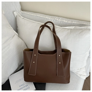Detailed view of brown tote bag with white stitching and decorative gold studs