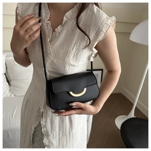 Détail d'un mini sac bandoulière noir avec boucle dorée porté par un mannequin en intérieur