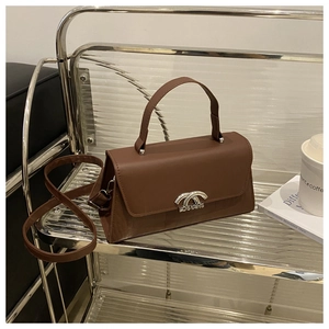 Close-up of brown leather crossbody bag with silver engraved buckle on metal shelf