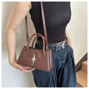 Détail d'un sac à main marron foncé avec étoile argentée et bandoulière réglable