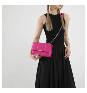 Model wearing a vibrant magenta crossbody bag with gold chain strap and metal buckle