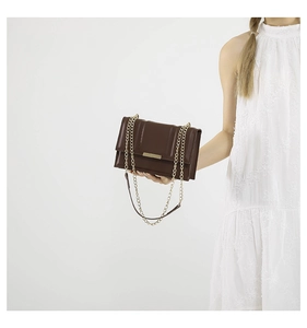 Detail of a dark brown crossbody bag featuring vertical embossed texture and golden chain