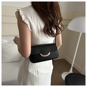 Sac bandoulière minimaliste en cuir noir avec une boucle dorée distinctive en demi-lune