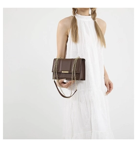 Detail of dark brown faux leather chain bag with gold metal buckle on white dress