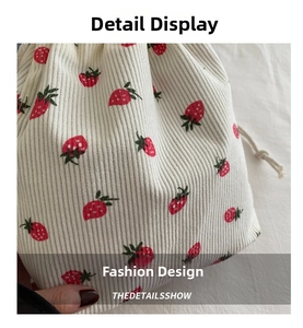 Close-up of beige corduroy bucket bag featuring red strawberry print and drawstring detail