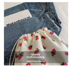 Detail of white corduroy drawstring bucket bag featuring fresh red strawberry patterns