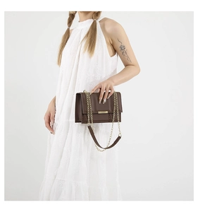 Detail of a brown leather crossbody bag with gold chain strap and metallic bar closure