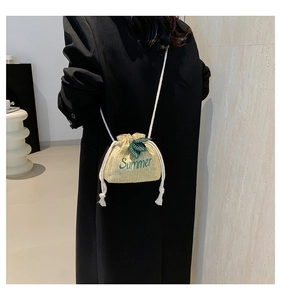 Detail of summer straw bucket bag with green leaf embroidery and white braided rope strap