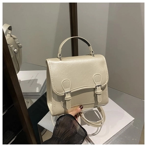 Detail of cream flap backpack showing top handle and buckle straps on textured leather