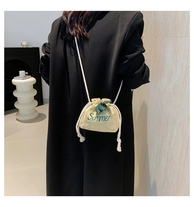 Detail of straw woven bucket bag featuring green Summer embroidery and cotton rope drawstring