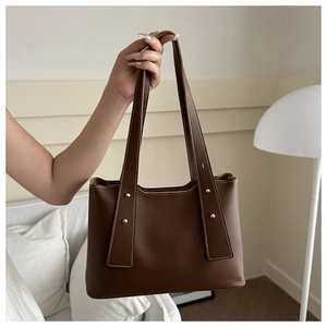 Detail of dark brown tote bag featuring white contrast stitching and gold metal rivets