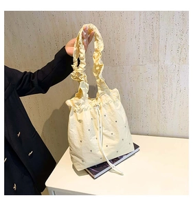 Detail of light yellow drawstring tote bag with ruffle strap and sparkling metal studs