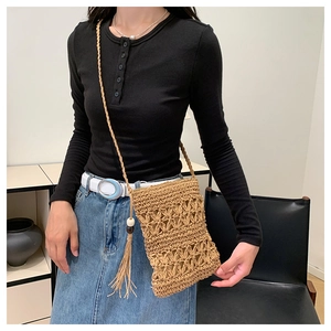 Detail of hand-woven straw crossbody bag with hollow diamond pattern and tassel