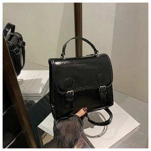 Detailed mirror reflection of a black glossy satchel bag with dual metal buckles