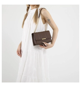 Detail of brown quilted leather bag with gold metal clasp and chain strap on white dress