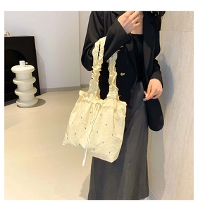 Close-up of cream drawstring tote bag featuring rhinestone accents and ruffled shoulder straps