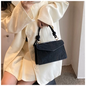 Detail of black pleated texture handbag with woven knot handle and gold metal rings