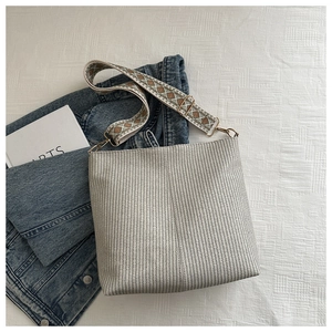 Detail of beige woven bucket bag featuring a vintage geometric pattern wide shoulder strap