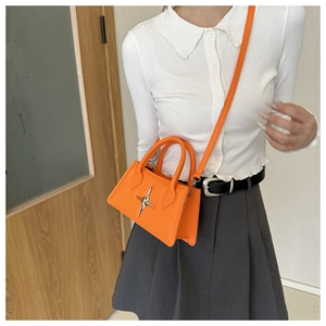 Petit sac à bandoulière orange vif avec ornement d'étoile argentée sur chemise blanche