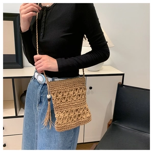 Detail of straw crossbody bag with floral weave patterns and decorative tassel charm