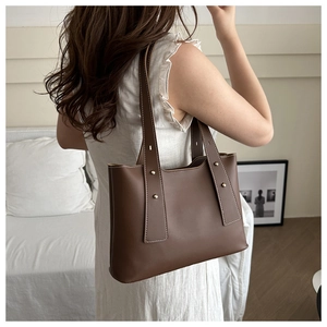 Brown leather tote bag with contrast stitching and gold rivets worn by a model