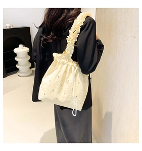 Detail of beige drawstring bucket bag featuring pearl beads and ruffled shoulder strap