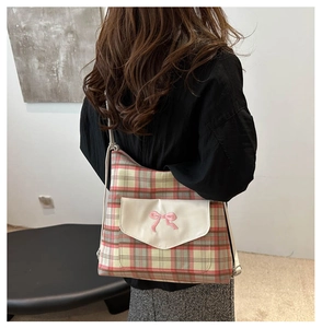 Detail of vintage plaid shoulder bag featuring pink bow embroidery on a canvas front pocket