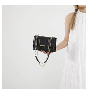 Detail of black quilted shoulder bag with gold chain strap and metallic closure