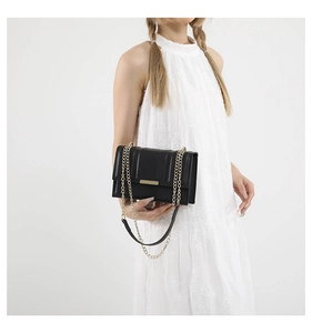 Detail of black crossbody bag with gold hardware and vertical stitching on white dress