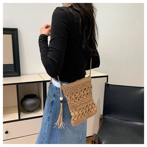 Detail of woven straw crossbody bag featuring floral hollow patterns and side tassels