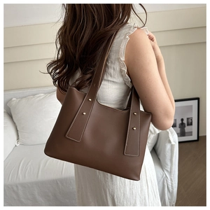 Detail of dark brown leather tote bag with gold studs on white lace dress background