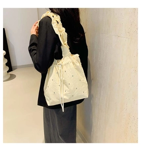 Detail of ruffled shoulder strap and silver rhinestones on cream drawstring tote bag