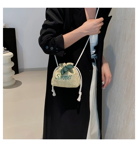 Detail of straw bucket bag with green Summer embroidery and leaf charms on shoulder