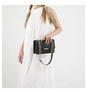 Detail of elegant black crossbody bag with gold chain strap worn on white dress