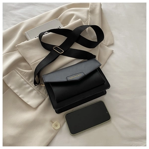 Close-up of small black crossbody bag with gold lettering shown next to a smartphone