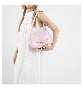 Gros plan d'un sac à bandoulière en cuir verni rose avec nœud sur une robe en dentelle