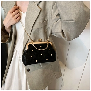 Dettaglio di una pochette nera vintage con rivetti a cuore dorati e catena su modella