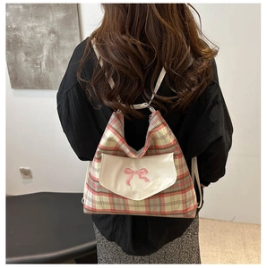 Detail of the pink and green plaid backpack featuring a white embroidered bow flap
