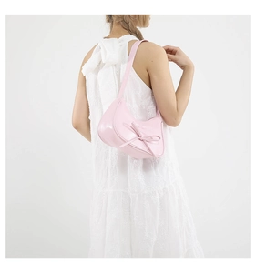 Détail du sac baguette rose à nœud sur l'épaule avec une robe en dentelle blanche