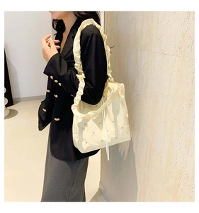Detail of cream pleated tote bag featuring rhinestone embellishments and a soft shoulder strap