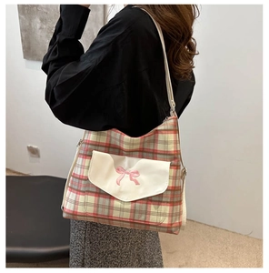 Detail of pink plaid tote with bow embroidery and cream flap pocket on model