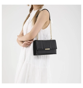 Detail of black quilted leather shoulder bag with gold chain strap on a white dress