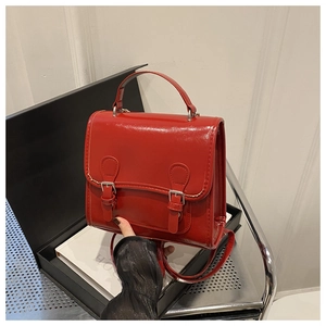 Detail of red glossy patent leather backpack with yellow stitching and silver buckles