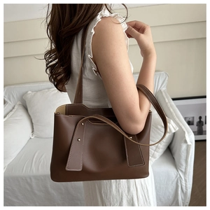 Brown leather tote bag with gold studs and stitching shown in a lifestyle home setting