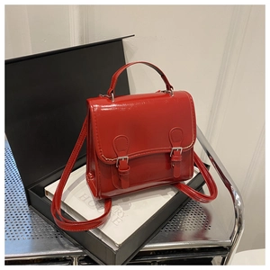 Detail of red glossy patent leather handbag with polished metal buckles and precise stitching