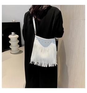 Detailed view of white leather crossbody bag with gold studs and long fringe tassels