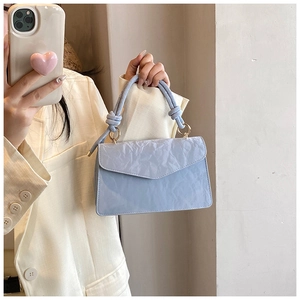 Detail of light blue textured handbag featuring a knotted handle and gold metal hardware